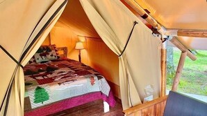 Ein gemütliches Zelt mit Bett, Lampe und Blick ins Freie.