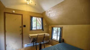 Eine kleine, einräumige Holzhütte mit Holzboden, Schreibtisch, Stuhl und Bett.