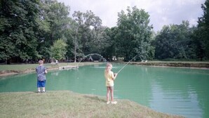 A pond with two people fishing, surrounded by trees.