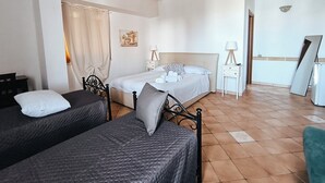 A bedroom with two beds, a wooden ceiling, a painting on the wall, and a mirror leaning against the wall. - Avola Opera House (Avola)