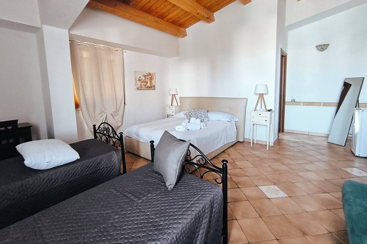 A bedroom with two beds, a wooden ceiling, a painting on the wall, and a mirror leaning against the wall.
