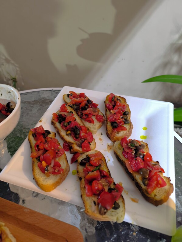 A white plate with several pieces of toast topped with tomatoes, olives, and mushrooms.