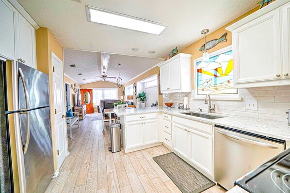 A spacious kitchen with white cabinets, a stainless steel refrigerator, and a large window with a stained glass design.