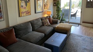 Ein Wohnzimmer mit einem grauen Sofa, einem blauen Couchtisch und einer Tür, die auf eine Terrasse im Freien führt.