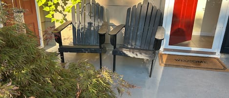 A wooden bench and chair outside a building with a red door and a welcome mat.