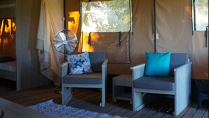 A cozy room with a bed, two armchairs with cushions, a fan, and a window with a view of trees.
