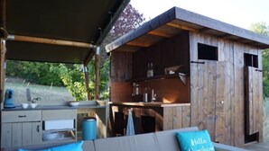 A wooden cabin with a kitchenette, a sofa with a blue pillow, and a view of greenery outside.
