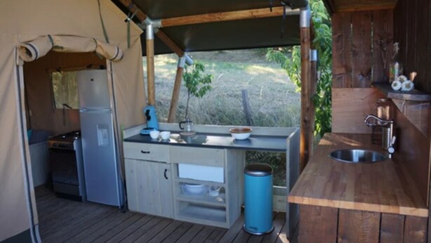 A compact kitchen with a stove, refrigerator, and sink, surrounded by wooden walls and a tent-like structure.