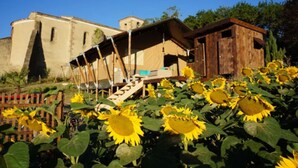 A rustic wooden structure with a staircase leading to a covered area, surrounded by sunflowers.