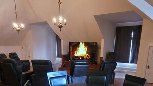 A dining area with a round table and chairs, a fireplace, and a high ceiling with chandeliers.