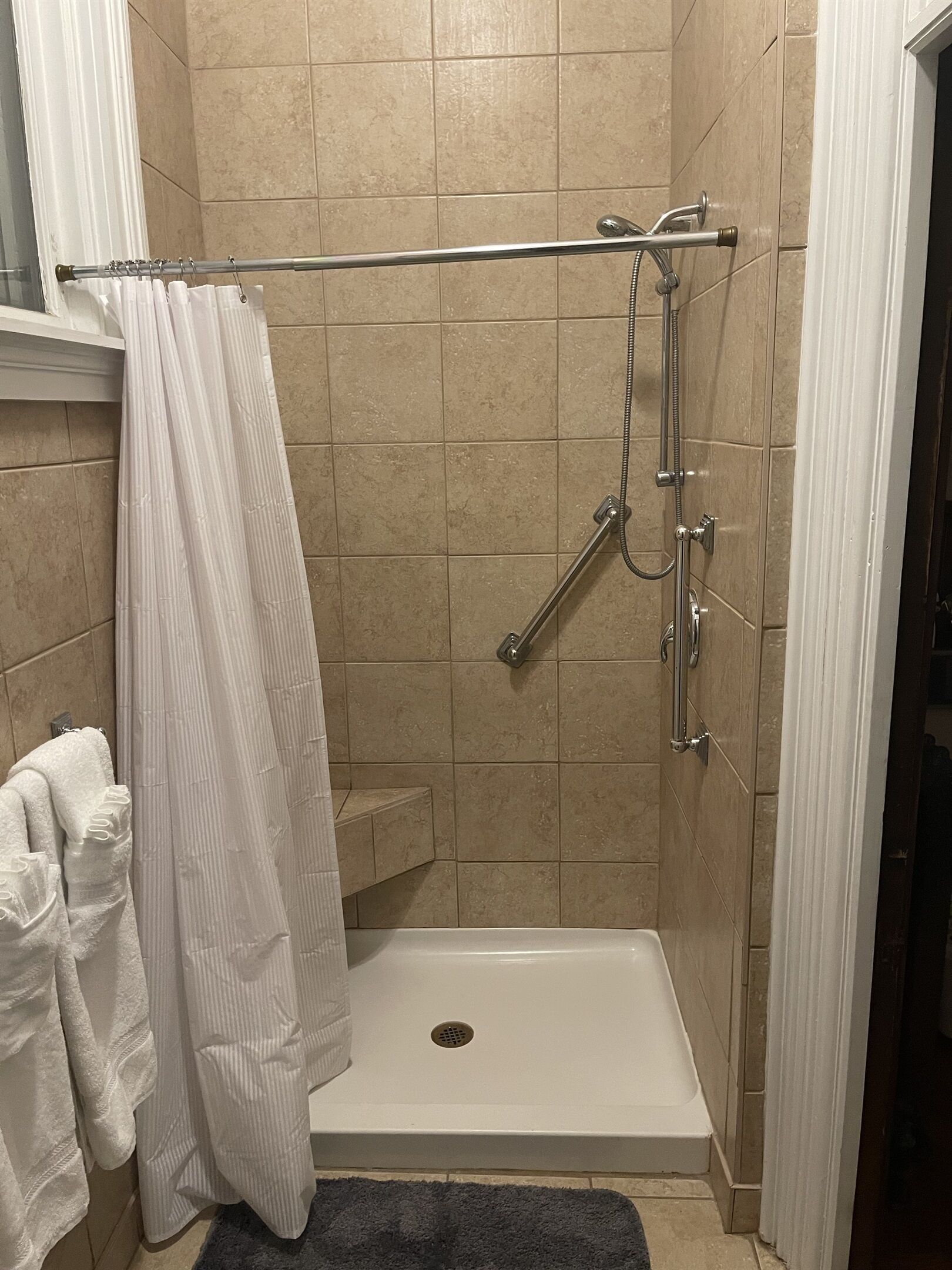 Ein Duschbereich mit einer weißen Badewanne, einer Duschbrause und einer Haltestange.