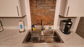 A kitchen with a stainless steel sink, white cabinets, a brick backsplash, and a coffee maker.