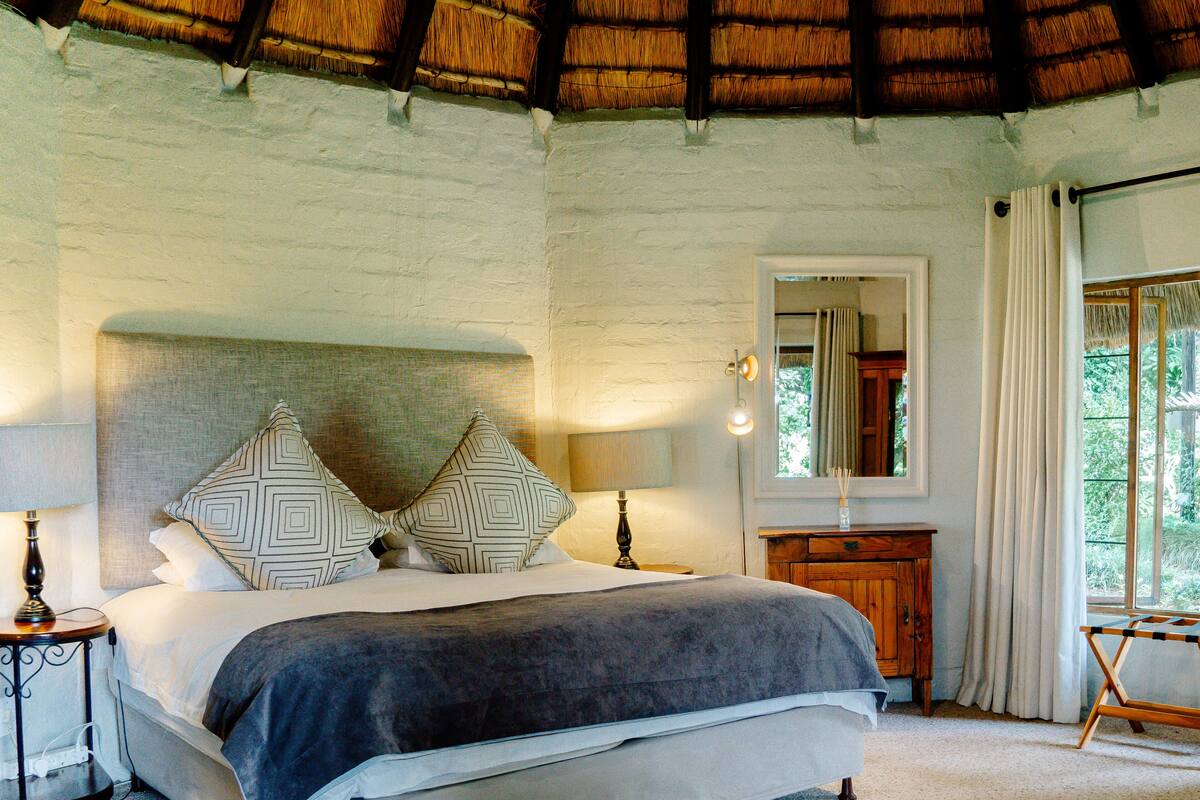 Un dormitorio con cama, lámparas de noche, mesita de noche, cómoda de madera, espejo y ventana con cortinas.