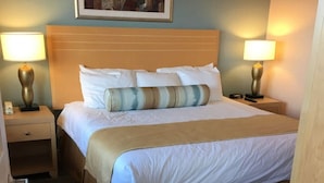 A hotel room with a large bed, two bedside tables with lamps, a painting on the wall, and a wooden floor.