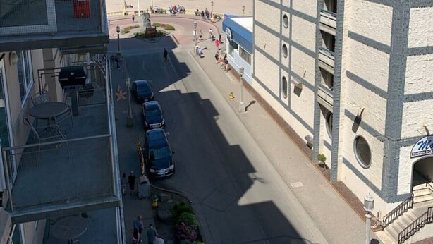 A coastal hotel with a view of the beach, a parking area, and a street with pedestrians.