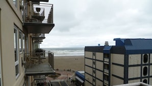 A view from a balcony overlooking a beach with a building featuring multiple balconies and a blue roof.