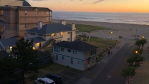 A coastal hotel with multiple buildings, a parking area, and a view of the beach at sunset.