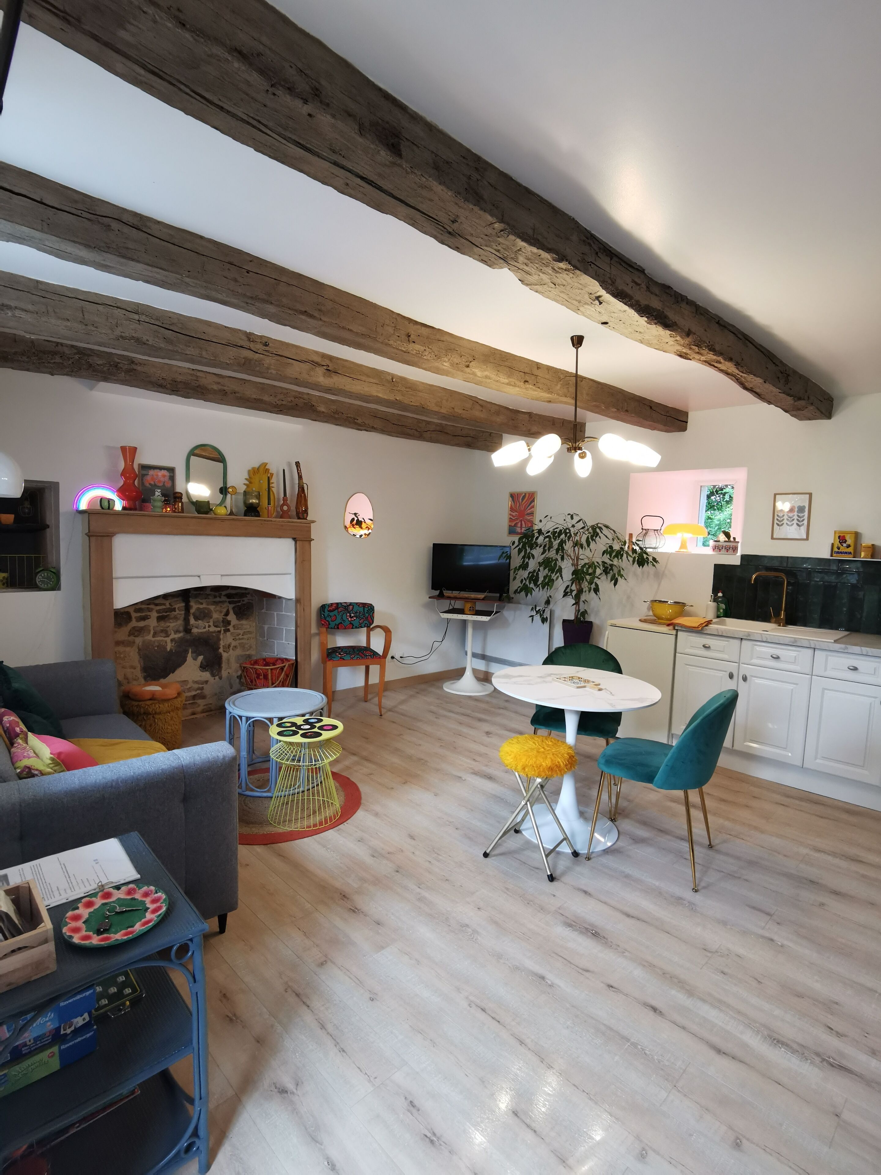 A living room with a fireplace, a dining area with a round table and chairs, and a kitchen with white cabinets.