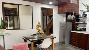 Eine kleine Küche mit Kühlschrank, Mikrowelle und Herd. Es gibt einen Essbereich mit Tisch und Stühlen sowie eine Treppe, die zu einer oberen Ebene führt.