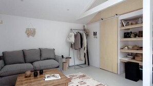 A living room with a grey sofa, a wooden coffee table, and a black ottoman. There is a clothing rack with various garments and a mirror. A wooden shelf unit with decorative items is visible. - PYLA: Nice creative studio 200 m from the beach (La Teste-de-Buch)