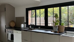 A modern kitchen with a black-framed window, a wooden stool, and a potted plant on the counter. - PYLA: Nice creative studio 200 m from the beach (La Teste-de-Buch)