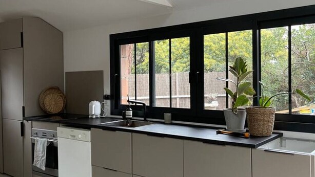A modern kitchen with a black-framed window, a wooden stool, and a potted plant on the counter. - PYLA: Nice creative studio 200 m from the beach (La Teste-de-Buch)