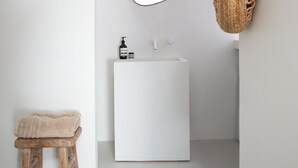 A minimalist bathroom with a white sink, a wooden stool, a hanging woven bag, and a round mirror. - PYLA: Nice creative studio 200 m from the beach (La Teste-de-Buch)