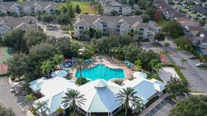 An aerial view of a resort with a central swimming pool, multiple buildings, and surrounding greenery.