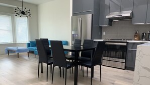 Una cocina moderna con comedor, que incluye una isla grande, electrodomésticos de acero inoxidable y un sofá azul al fondo.