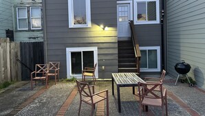 Una casa de dos plantas con un patio que incluye una mesa, sillas, una escalera de madera y una parrilla.