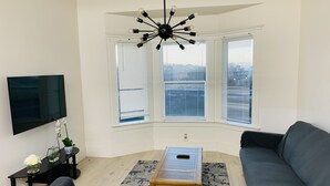 Una sala de estar moderna con un ventilador de techo negro, un televisor de pantalla plana, un sofá gris, una mesa de centro de madera y una alfombra azul estampada.