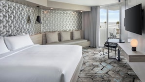 A modern hotel room with a large bed, a seating area with cushions, a dining table, and a TV mounted on the wall. - Renisassance Daytona Beach Oceanfront (Daytona Beach)