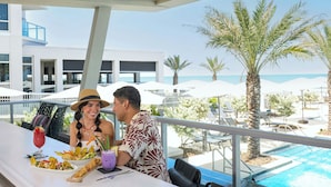 A dining area with a pool view, outdoor seating, and palm trees. - Renisassance Daytona Beach Oceanfront (Daytona Beach)