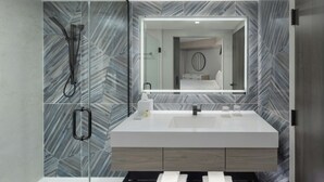 A modern bathroom with a glass shower enclosure, a white sink, and a mirror above it. - Renisassance Daytona Beach Oceanfront (Daytona Beach)