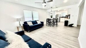 Un salon moderne avec un canapé bleu, une table à manger et un coin cuisine à l’arrière-plan.