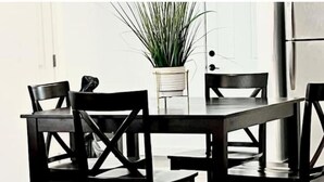Un coin repas avec une table rectangulaire et quatre chaises, une plante en pot et une porte en arrière-plan.
