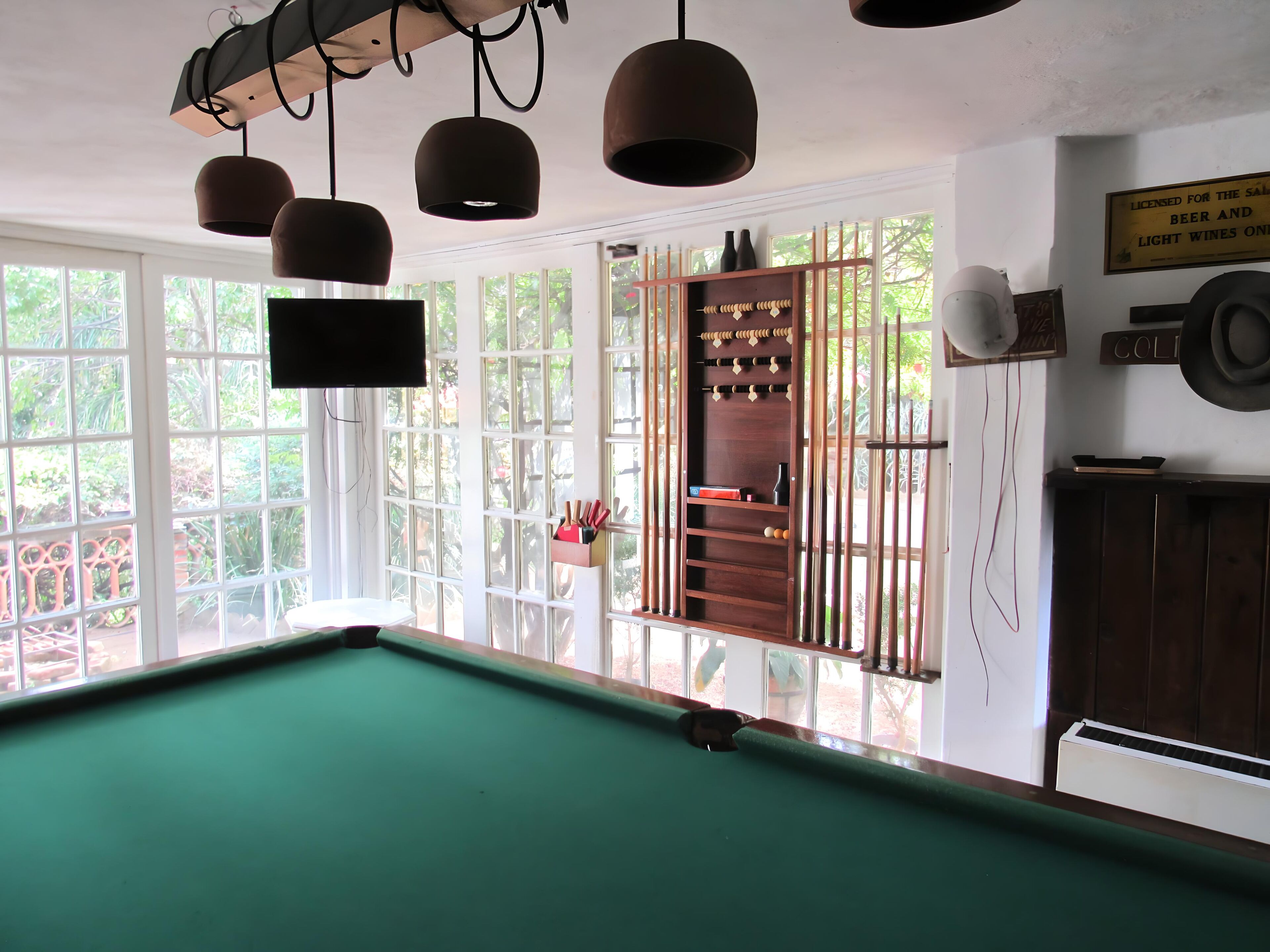 A billiards room with a pool table, hanging lights, and a wooden cabinet with bottles.