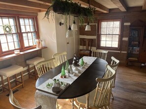 A dining area with a long table, white chairs, hanging plants, and a wooden ceiling. - Oak Haven 1827 Cabin Rental (Union Township)