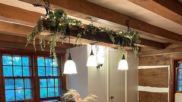 A dining area with a wooden table, white chairs, and a hanging plant decoration. - Oak Haven 1827 Cabin Rental (Union Township)