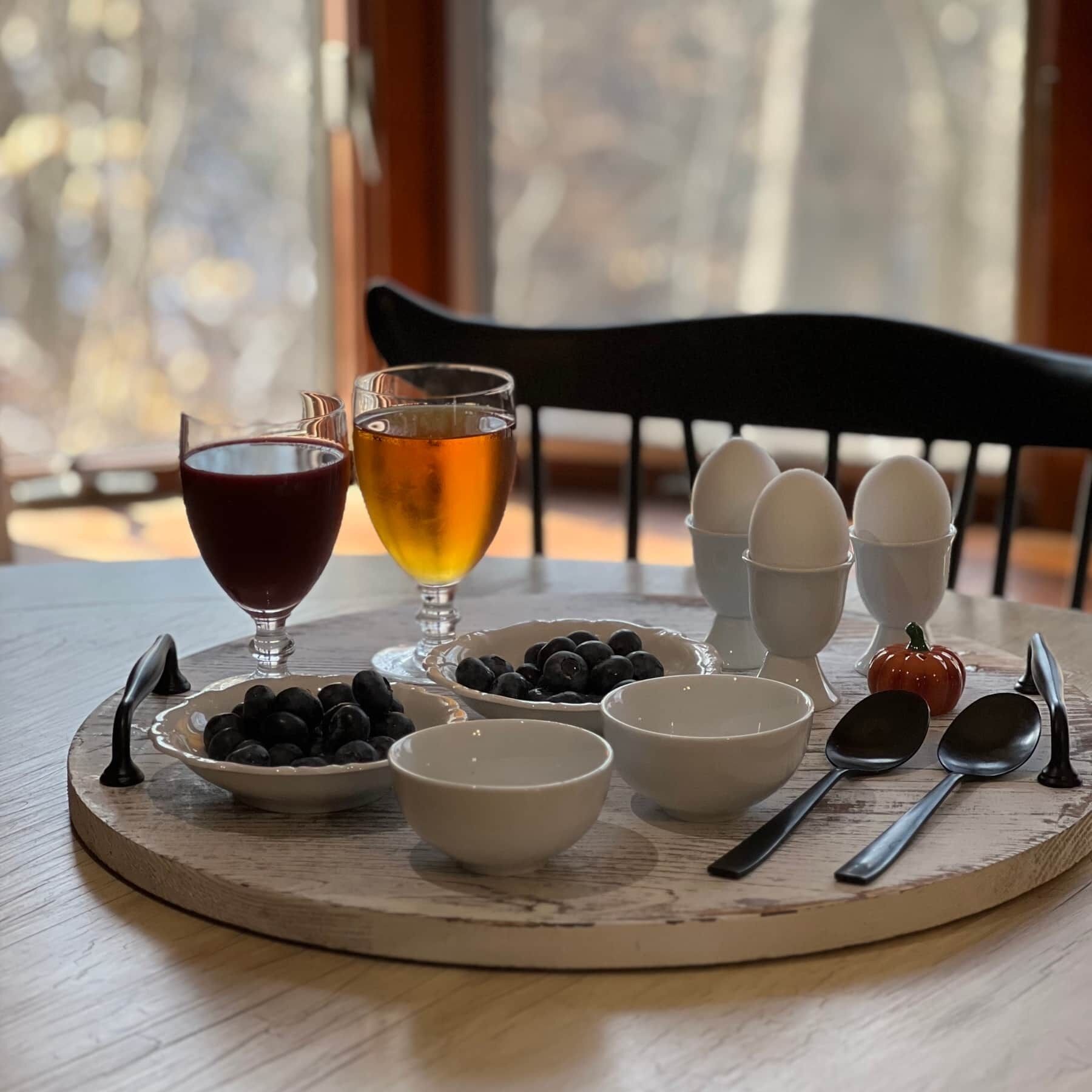 A breakfast setting with eggs, blueberries, and two glasses of beverages on a wooden table.