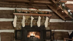 A stone fireplace with stockings hanging above, a wooden ceiling, and a table with a candle and a jar. - Oak Haven 1827 Cabin Rental (Union Township)