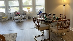 Een ruime woonkamer met een eethoek, grote ramen en een kroonluchter.