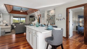 Un amplio espacio de estar con una isla grande, una mesa de comedor dispuesta con platos y vasos azules, y un sillón gris.