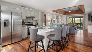 Una cocina moderna con electrodomésticos de acero inoxidable, una isla blanca con taburetes y una zona de comedor con platos azules.