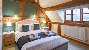 Une chambre avec un plafond en bois, un grand lit avec des oreillers, deux lampes de chevet, une fenêtre donnant sur un beau paysage et un radiateur.