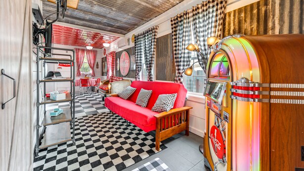Une pièce à l’ambiance rétro, avec un canapé rouge, un sol à carreaux, un juke-box et un décor d’époque.