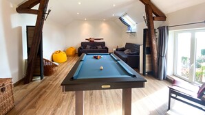Une table de billard dans une pièce dotée d’un plafond en pente, de deux canapés et d’une grande fenêtre.