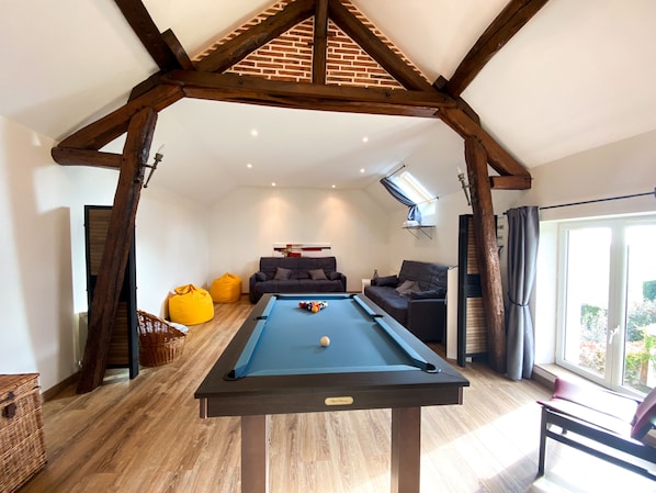 A pool table in a room with a sloped ceiling, two sofas, and a large window.