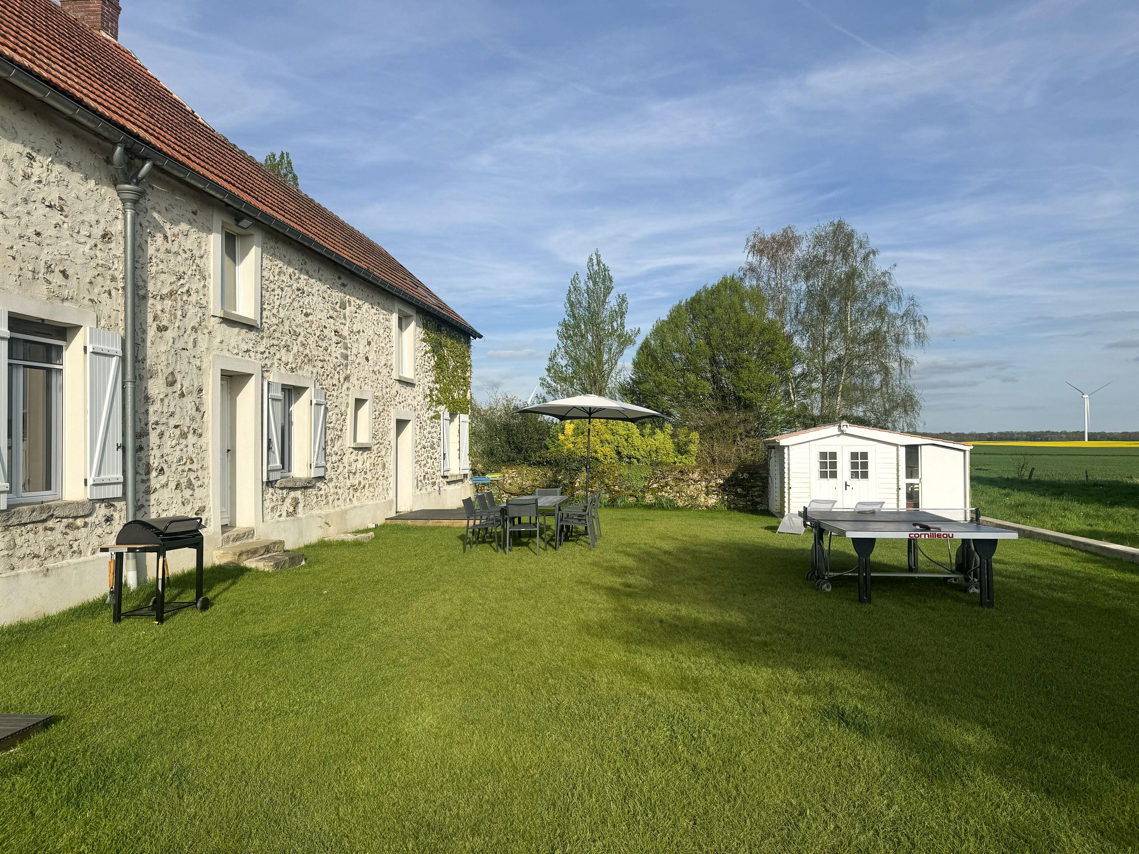 A stone building with a red-tiled roof, a grassy yard, and a small white shed.