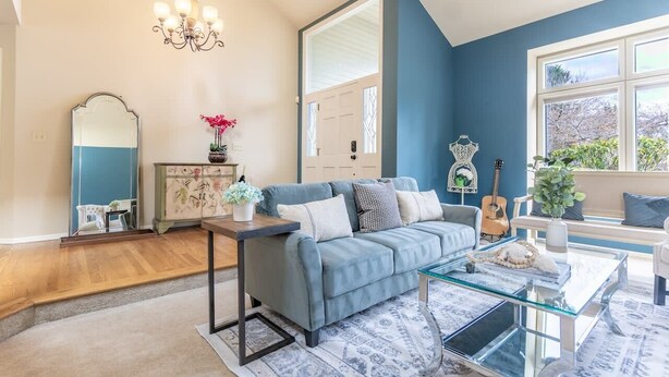 A living room with a blue sofa, a glass coffee table, a chandelier, a mirror, and a guitar.
